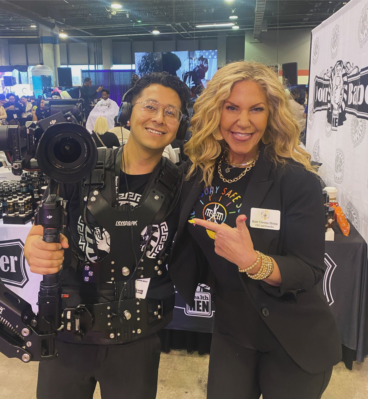 Brayan Olea, founder and creative director of Olea Productions, wearing a camera stabilizer rig while filming at a live barber industry event, alongside barber instructor Kate Owens Heins