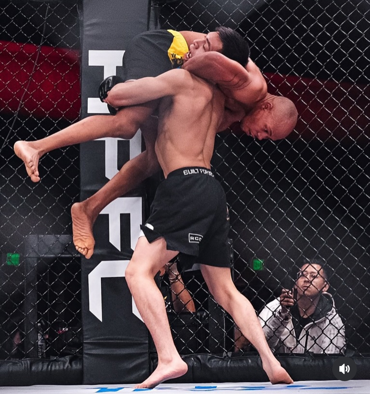 MMA fighter lifting an opponent inside the cage at a live fight event