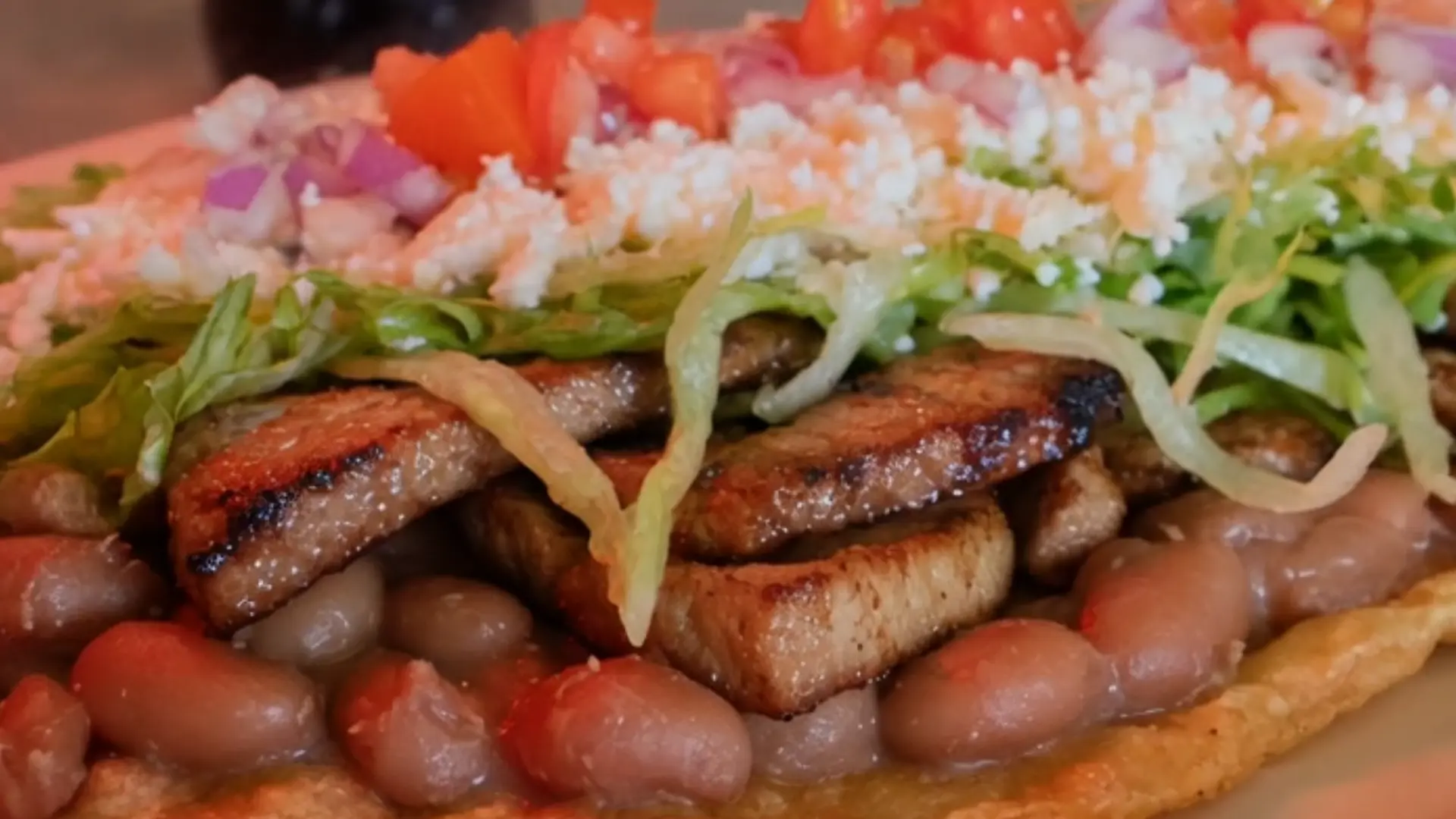 Close-up of a dish topped with beans, grilled meat, lettuce and tomatoes